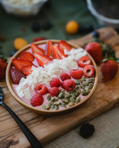 Smoothie bowl aux fruits rouges avec des toppings fraises, framboises, graines de courge et coco râpés